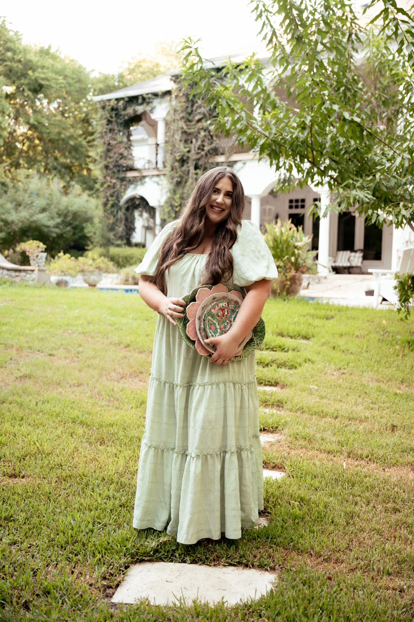 Alexandra standing outdoors holding a stack of decorative plates