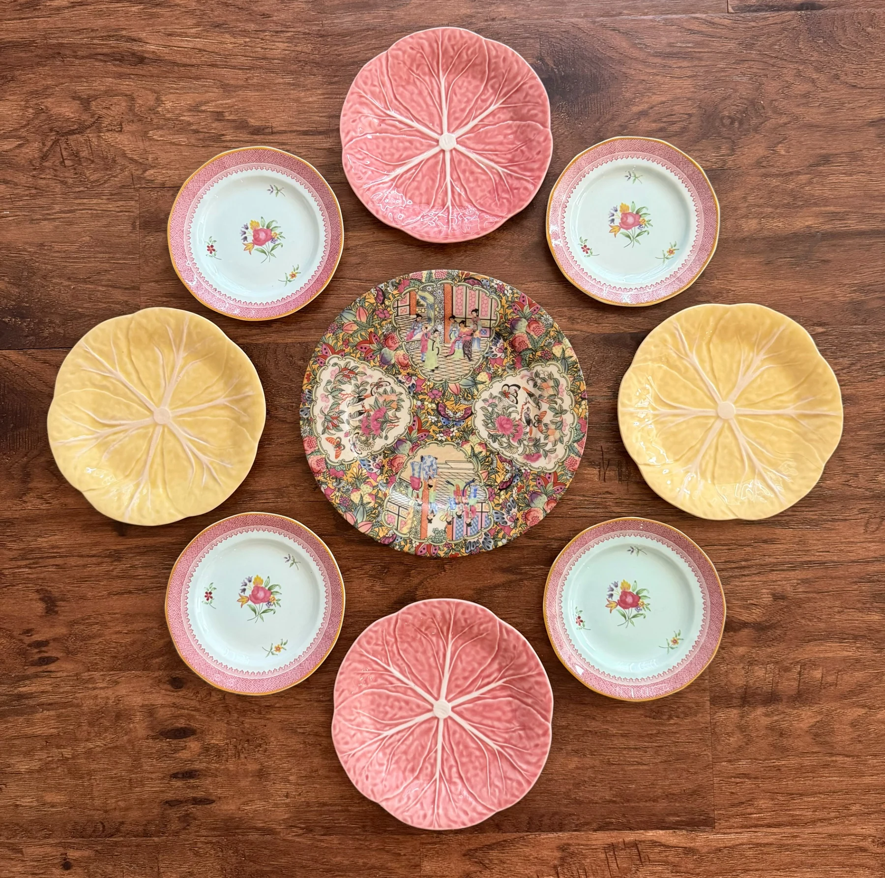 Pink, yellow and floral plate arrangement laid out on a wood floor